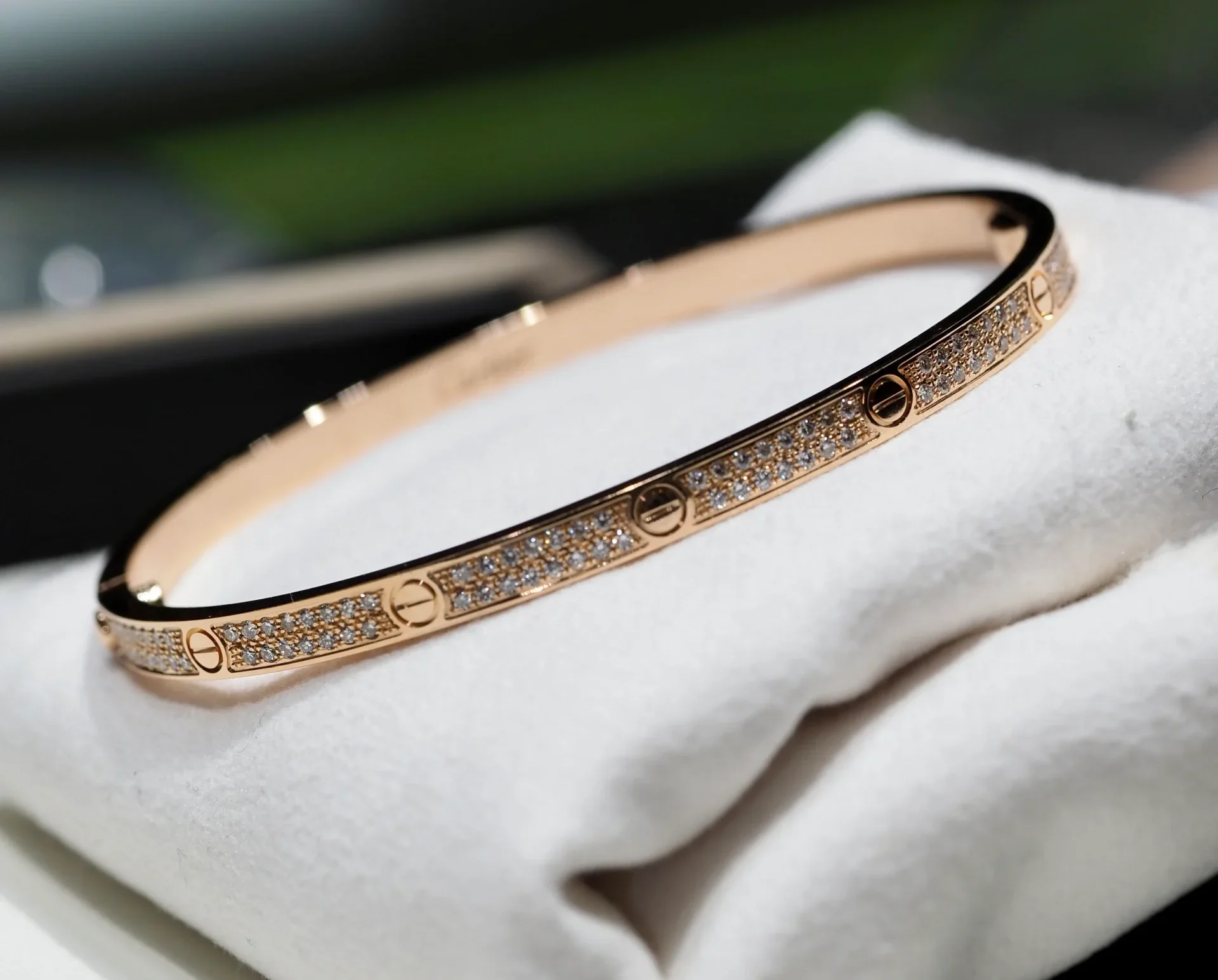 Shiny Cartier Love bracelet with diamonds sitting on a soft cushion